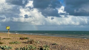 A pebbled beach with a caution sign and a view of the ocean under a cloudy sky.