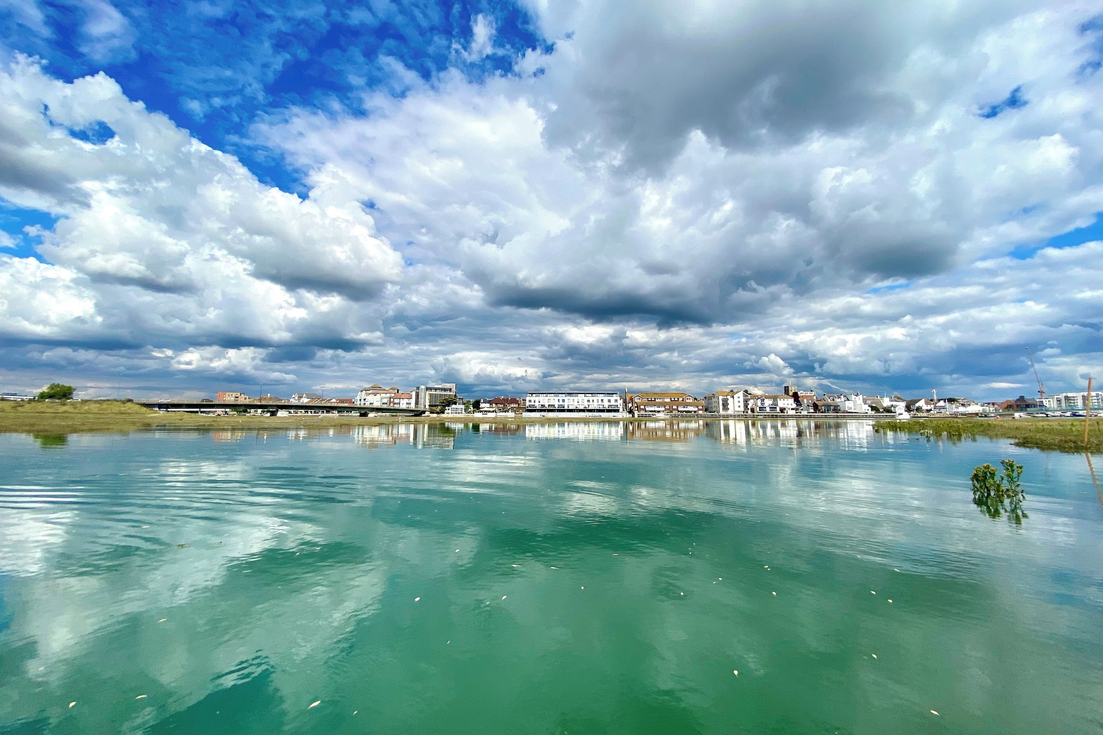 Ruhige Wasserfläche, die Gebäude und einen bewölkten Himmel spiegelt.