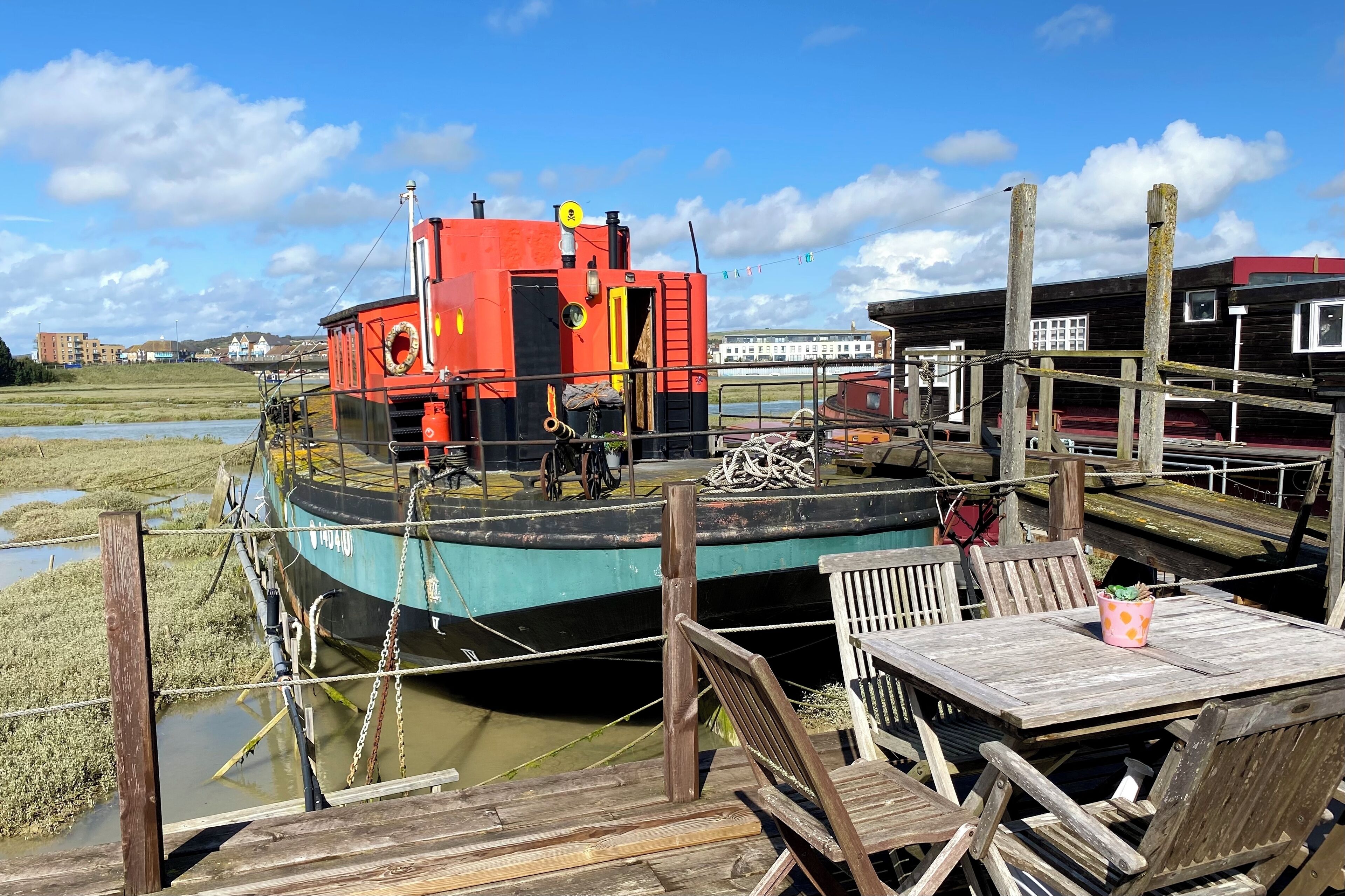 Une jetée avec un bateau rouge, des chaises en bois et une table.