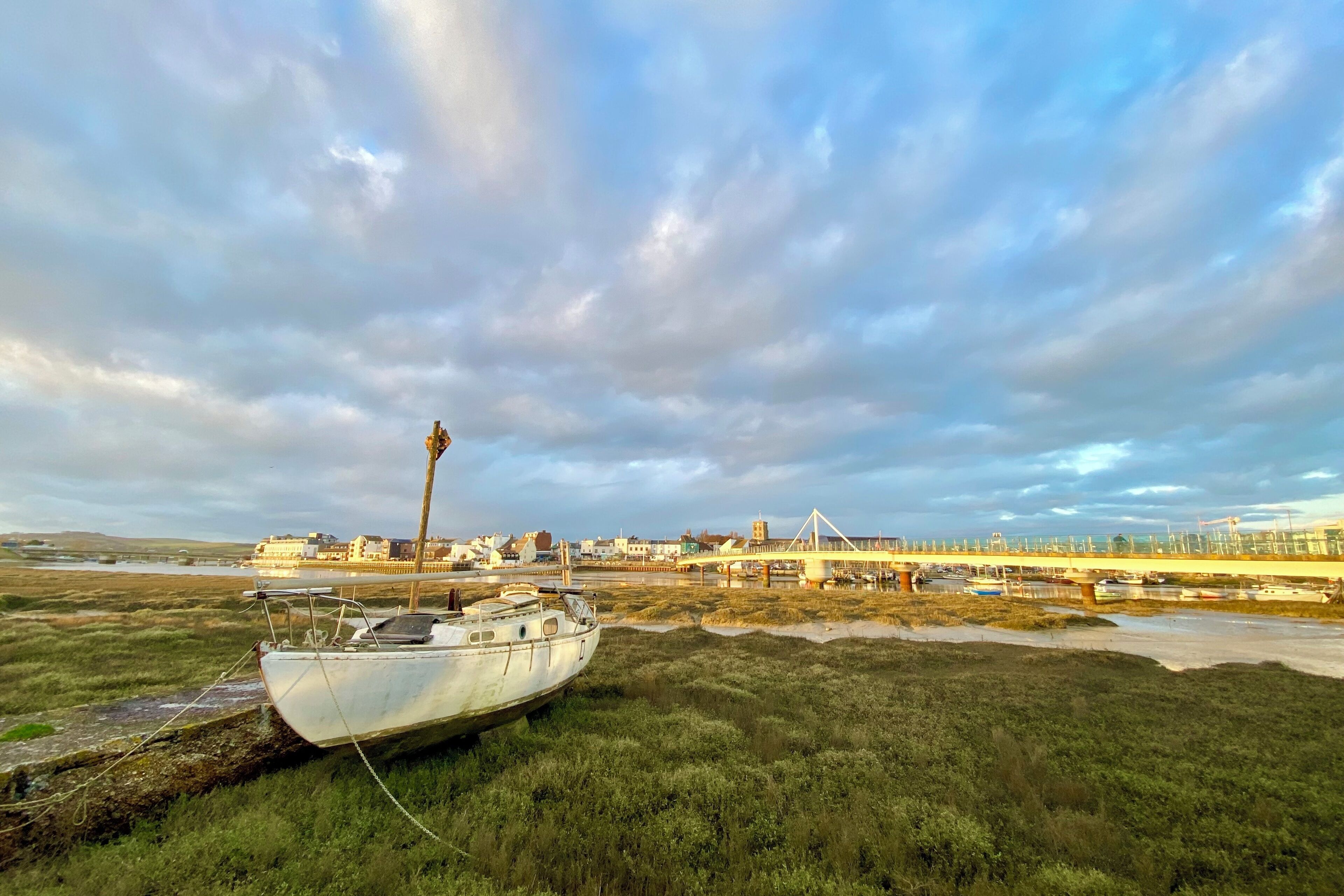 A boat stranded in a marshy area with a bridge and industrial buildings in the background.