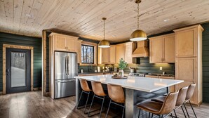 Eine moderne Küche mit Holzausstattung, einem Edelstahl-Kühlschrank, einer großen Kücheninsel mit Barhocker und Pendelleuchten.