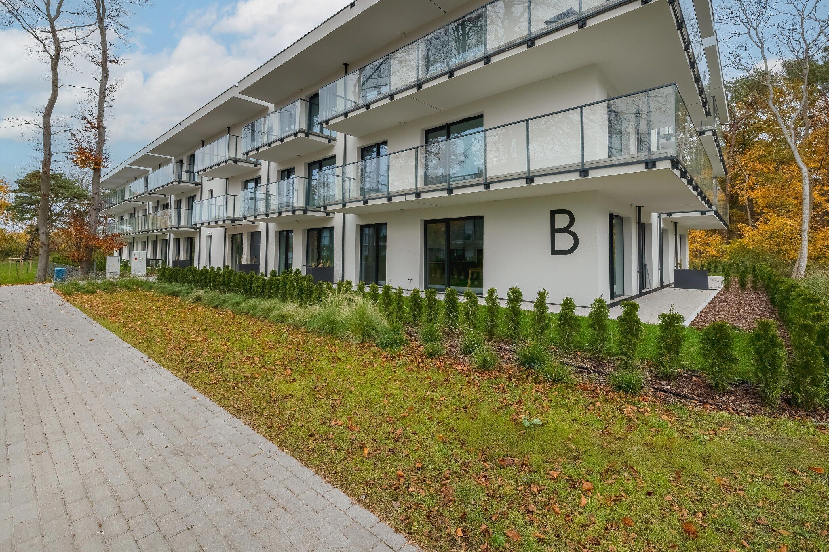 A modern multi-story building with balconies, a paved walkway, and landscaped areas.