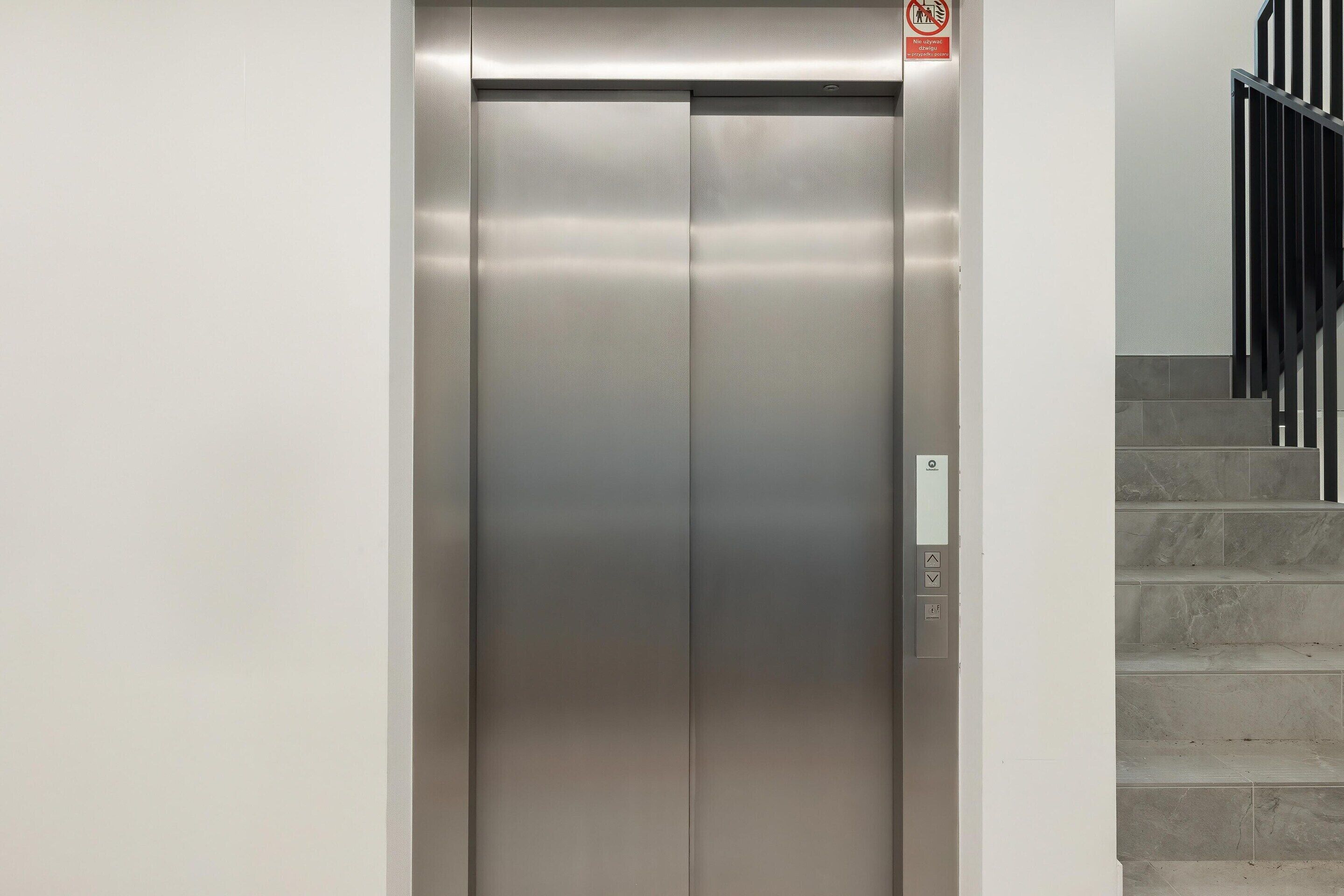 An elevator with a metallic finish, a control panel with buttons, and a no-smoking sign above it.