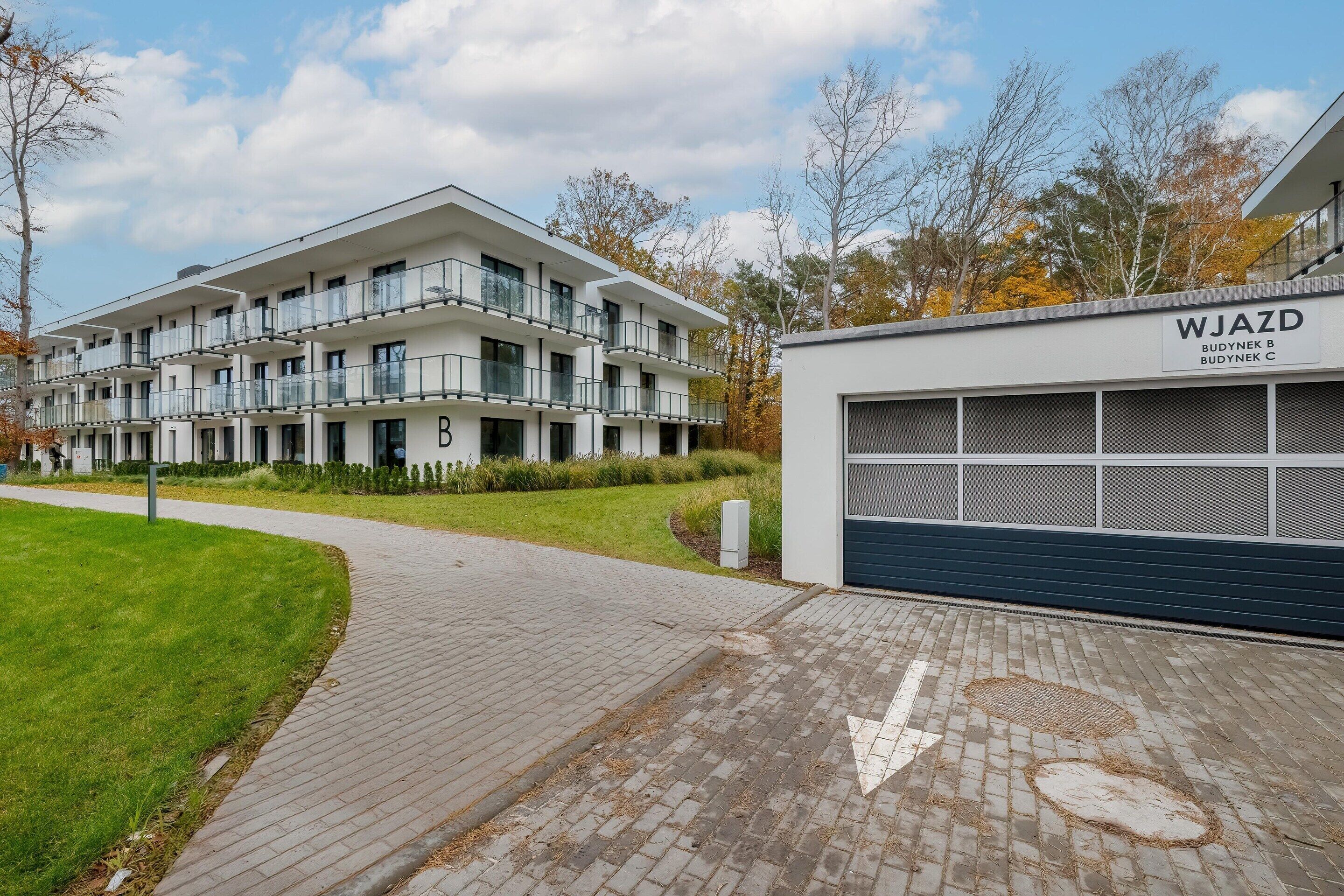 Um edifício moderno de vários andares com teto plano, varandas, calçada e garagem com placa.