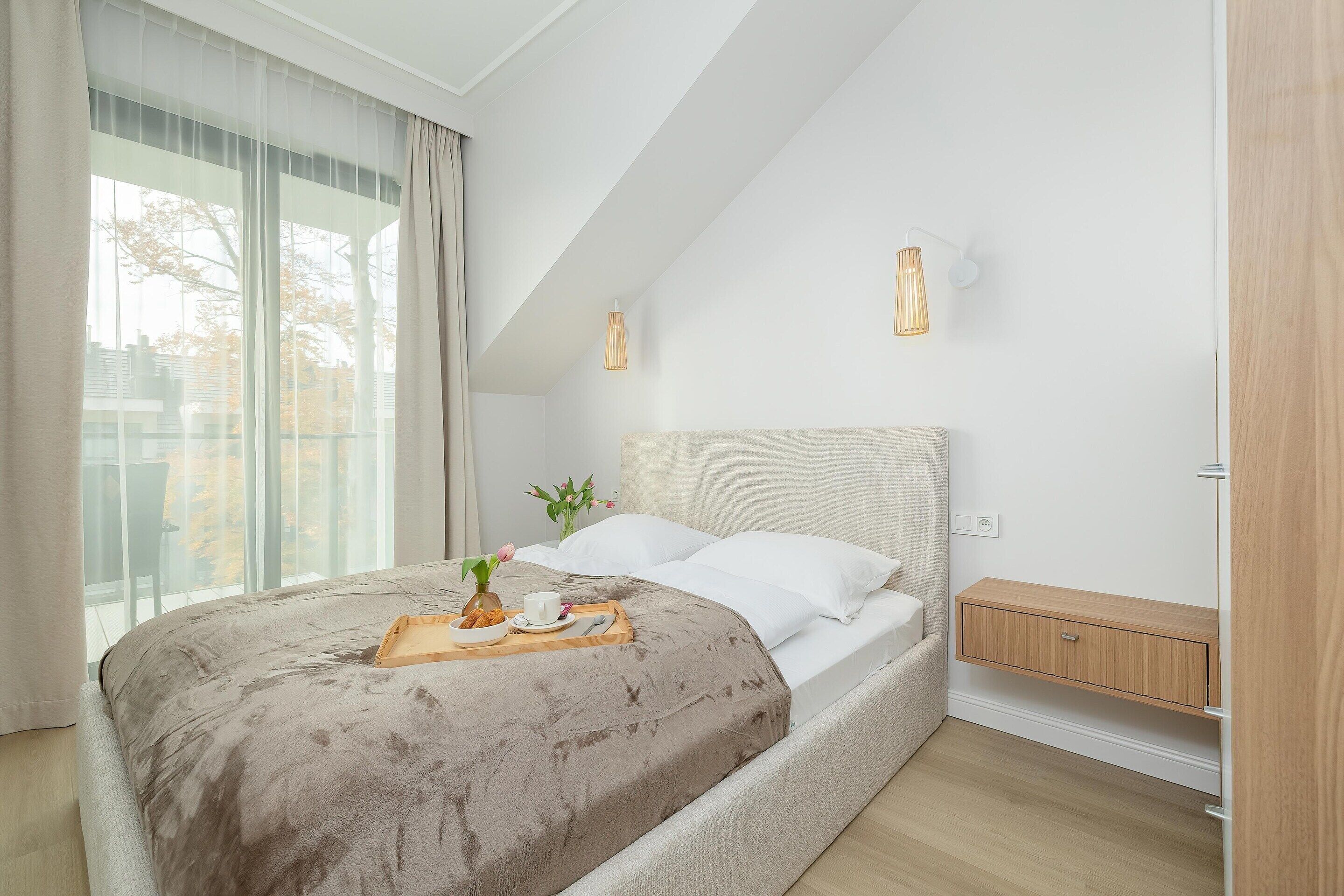 A modern bedroom with a large bed, a bedside table, and a window with curtains.