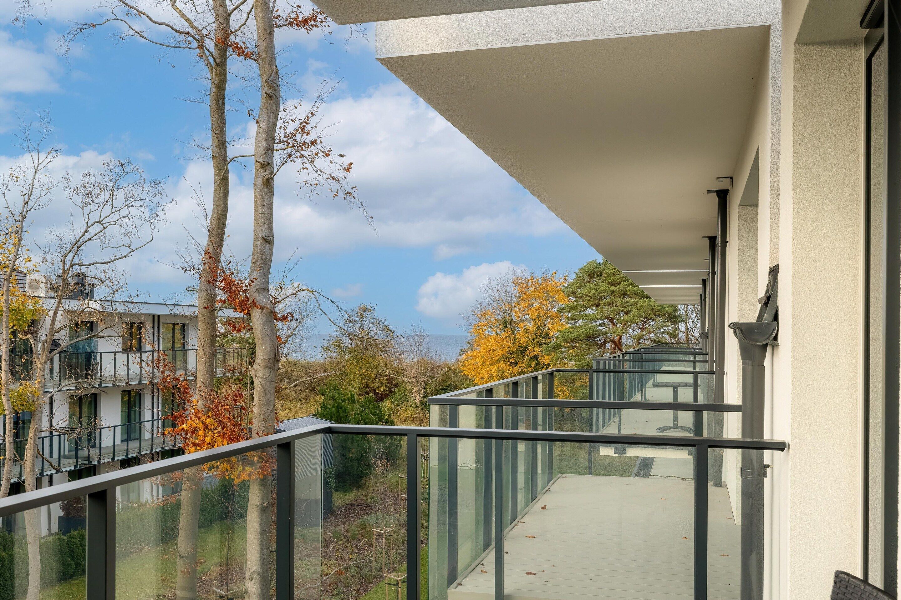 A modern building with a glass balcony overlooking a garden and trees.