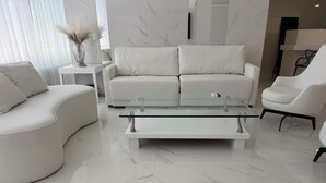 Ein modernes Wohnzimmer mit einem weißen Sofa, einem Glastisch und einem weißen Sessel.