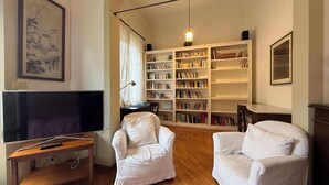 A living room with a television, white armchairs, a bookshelf, and a hanging light fixture. - Zanobi 75 - Three Bedroom Apartment, Sleeps 7 (Firenze)