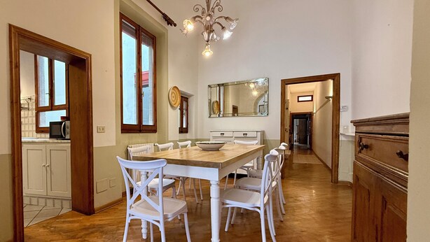 A dining area with a wooden table and white chairs, a chandelier, and a kitchen visible through an open door. - Zanobi 75 - Three Bedroom Apartment, Sleeps 7 (Firenze)