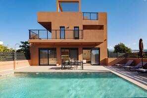 Um edifício moderno de dois andares com piscina, área de estar externa e vista para a paisagem.