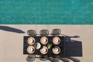 Mesa com seis cadeiras e uma planta central, com vista para a piscina.