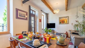 Un coin repas avec une table en bois mise pour le petit-déjeuner, un téléviseur et un canapé en arrière-plan.