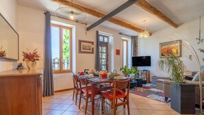 Un coin repas avec une table en bois, des chaises, un téléviseur et une plante.