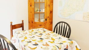 Ein Esstisch mit einem Tischlein mit Vogelmuster, zwei Holzsessel, ein Holzschrank mit Glastüren und eine Karte an der Wand.