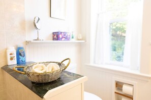 Un baño con una cesta de mimbre que contiene toallas blancas sobre una encimera de mármol, un espejo y una ventana con vistas a la vegetación.