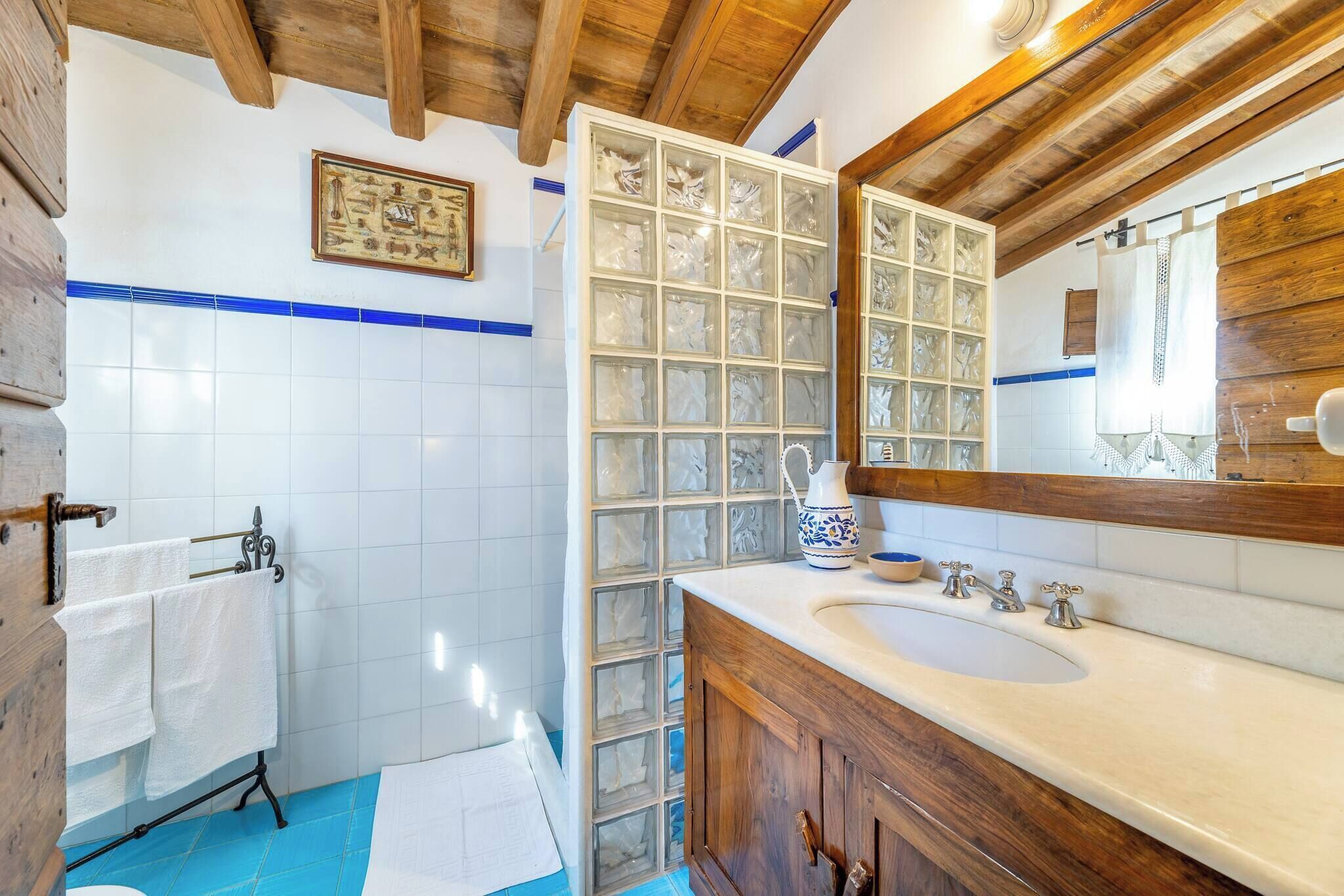 Een badkamer met een houten plafond, witte betegelde wanden, een grote spiegel en een houten wastafelmeubel met een wastafel.