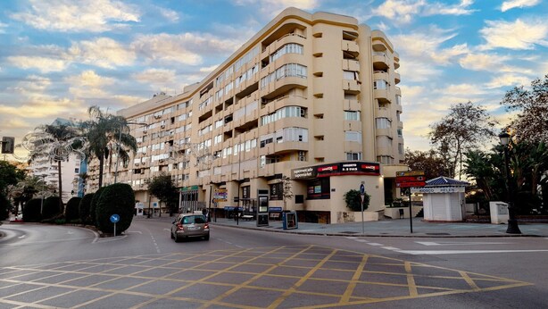 A multi-story hotel with a curved facade, a supermarket, and a small kiosk. - Beachfront Marbella Apartment With Balcony (Marbella)