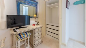 A small room with a television, a desk with a lamp, a chair, a wardrobe, and a mirror. - Beachfront Marbella Apartment With Balcony (Marbella)