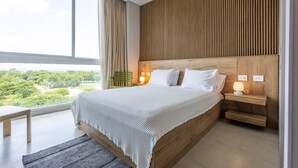 Ein modernes Schlafzimmer mit einem großen Bett, einem Holzkopfende, Nachttischen und Blick auf Grünfläche.
