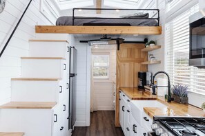A compact kitchen with a built-in stove, wooden cabinets, and a skylight above the sleeping area. - Pet-Friendly Zion Tiny Home • Private Hot Tub (Apple Valley)