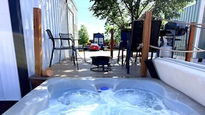 Een hottub met een houten terras, tuinmeubels en een barbecue.
