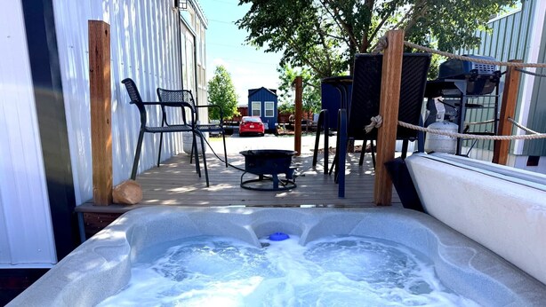 Een hottub met een houten terras, tuinmeubels en een barbecue.