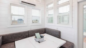 Een kamer met een witte tafel en een grijze bank, een raam met jaloezieën, en een airconditioning aan de muur.