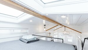 Een slaapkamer met dakraam, een bed met quilt, een hanglamp en uitzicht op buiten.