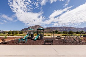 Un parque infantil con toboganes, columpios, bancos y montañas al fondo.