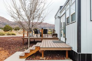 A modern building with a deck, outdoor seating, and a mountainous backdrop. - Pet-Friendly Zion Tiny Home • Private Hot Tub (Apple Valley)