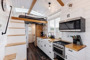 Bright full kitchen with gas range, microwave, farmhouse sink, and butcher block countertops. Stairs lead to the loft bedroom, maximizing space in this modern tiny home near Zion. - Pet-Friendly Zion Tiny Home • Private Hot Tub (Apple Valley)