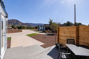 A patio area with a wooden deck, a small table, and a chair. - Zion Red-Rock Romance • Tiny Home + Private Deck (Apple Valley)