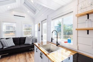 A modern kitchen with a black countertop, stainless steel sink, and a window overlooking a garden. - Zion Red-Rock Romance • Tiny Home + Private Deck (Apple Valley)