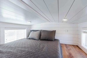 Et soveværelse med en seng, to puder, et vindue med persienner og et loft med indbygningsbelysning.