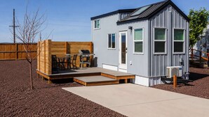 Ett litet hus i ett våningsplan med en uteplats, en grill och ett trädäck.