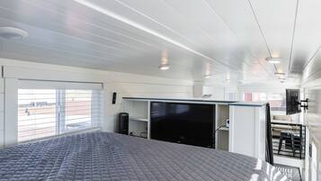 A modern interior with a bed, a TV, and a window with blinds.