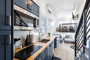 A modern kitchen with a built-in microwave, a sink, and a stove. There is a dining area with a table and chairs. - Zion Stay • Pet-Friendly Tiny Home (Apple Valley)
