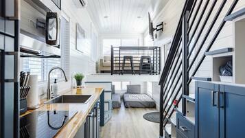 Open kitchen with bar seating, loft access, and views into the living and sleeping areas for an efficient tiny home layout.