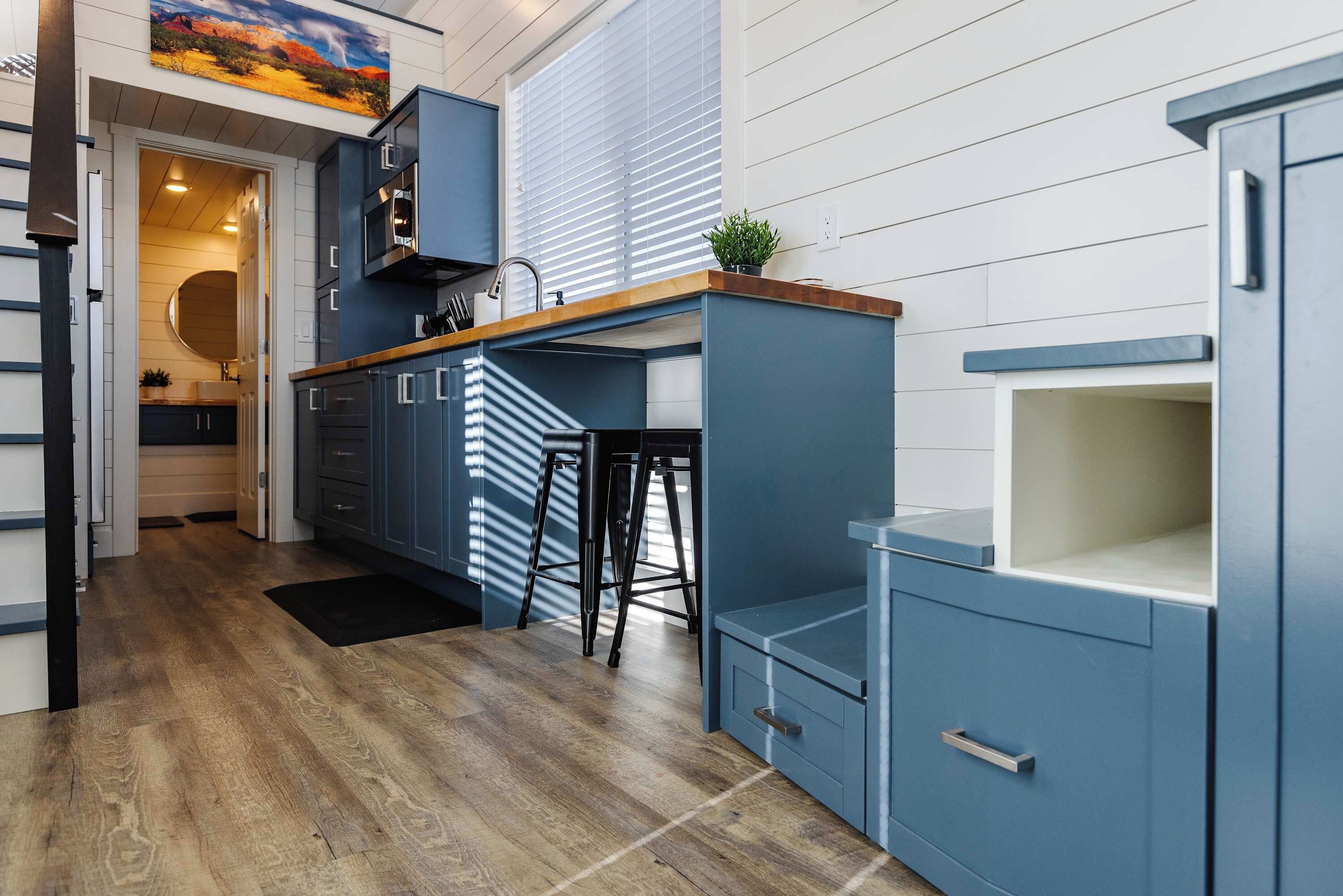 Well-designed kitchen with blue cabinetry, wood countertops, bar seating, and built-in storage in a bright, open tiny home interior.