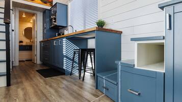 Well-designed kitchen with blue cabinetry, wood countertops, bar seating, and built-in storage in a bright, open tiny home interior.