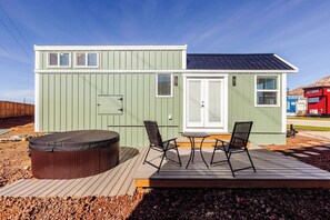 A small, single-story building with a deck, a hot tub, and two chairs. - Zion Hot Tub Tiny Home • Red Rock Views (Apple Valley)