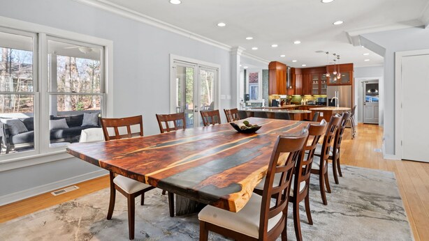 Un comedor amplio con una gran mesa y sillas de madera, una cocina al fondo y ventanas grandes con vistas al exterior.