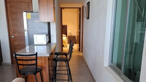 A compact kitchen with a refrigerator, microwave, and wooden cabinets. There is a dining area with two chairs and a small table. A window with a view of the outside is visible. - Apartment with a beautiful view of the Bay (Acapulco de Juárez)