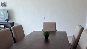 A dining area with a dark wooden table, beige upholstered chairs, and a small potted plant in the center. - Apartment with a beautiful view of the Bay (Acapulco de Juárez)