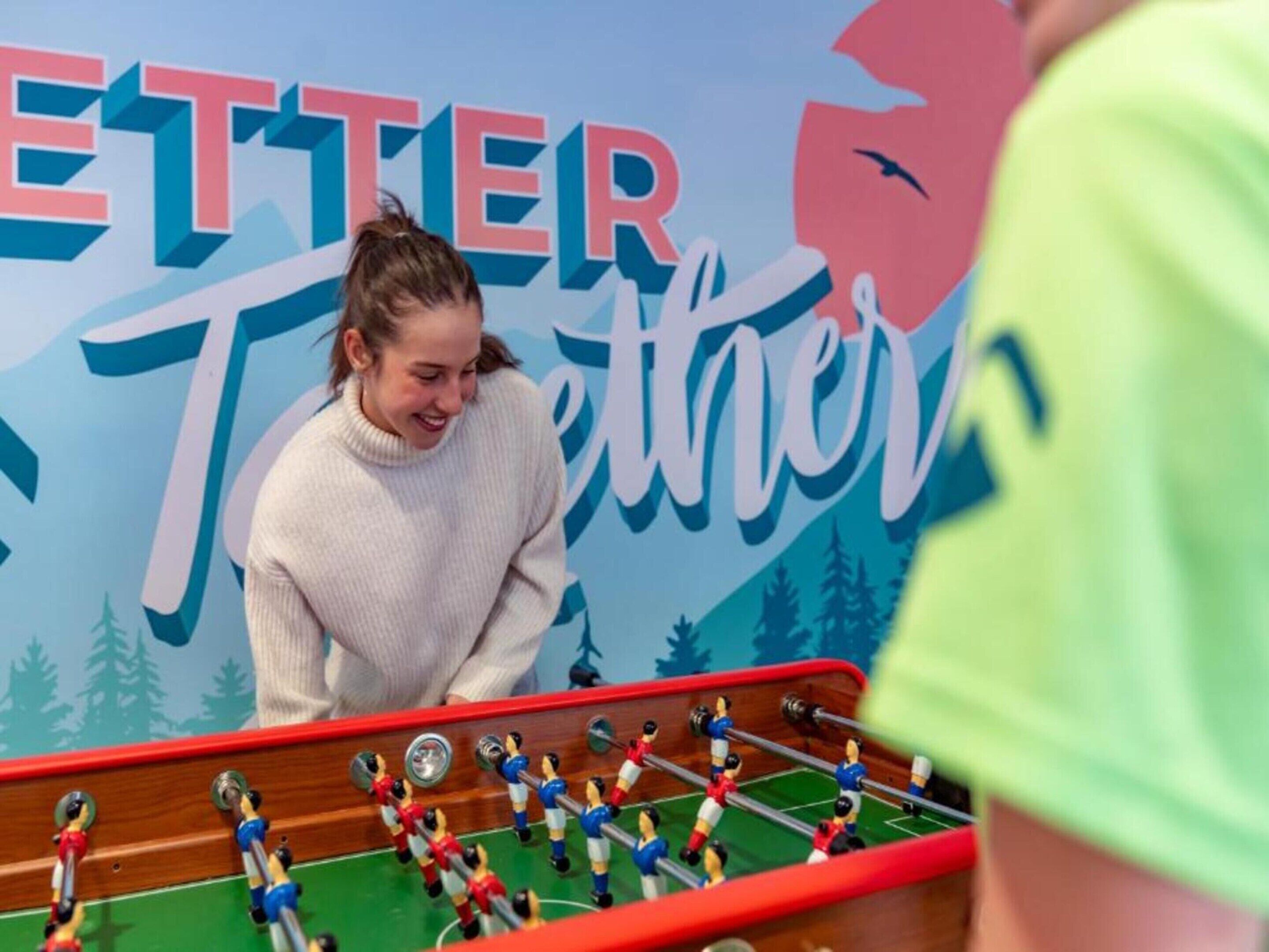 A person playing foosball in front of a wall with the text "ETTER Together".