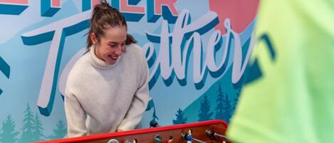 A person playing foosball in front of a wall with the text "ETTER Together".