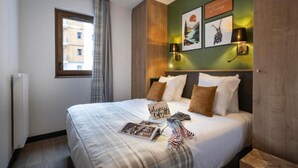 Quarto de hotel com uma cama grande, janela com cortinas, luminária fixada na parede e obras de arte emolduradas.