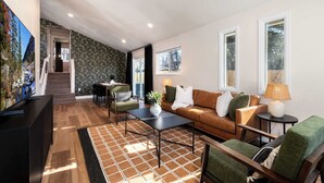 A modern living room with a sofa, coffee table, and a TV. There is a staircase leading to another level. - Arvada Retreat | Garage | Near Olde Town+Red Rocks (Arvada)