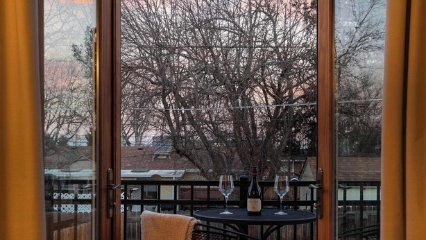 A wooden deck with a table and chairs, a bottle of wine, and two wine glasses. - Arvada Retreat | Garage | Near Olde Town+Red Rocks (Arvada)
