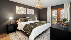 A bedroom with a bed, bedside lamps, a chandelier, artwork, a window with curtains, and a desk with a model airplane. - Arvada Retreat | Garage | Near Olde Town+Red Rocks (Arvada)
